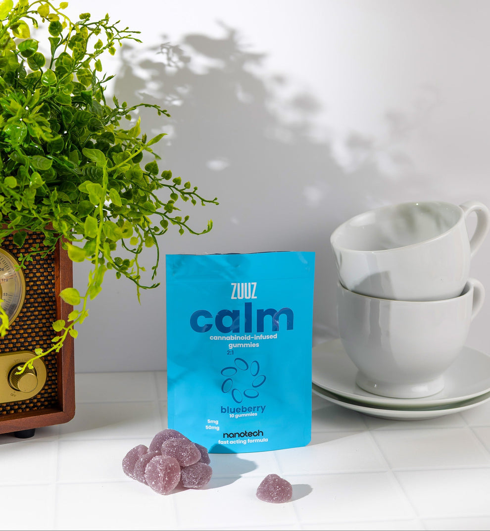 Zuuz Calm gummies packaging with purple gummies on a white surface with a plant and teacup in the background.